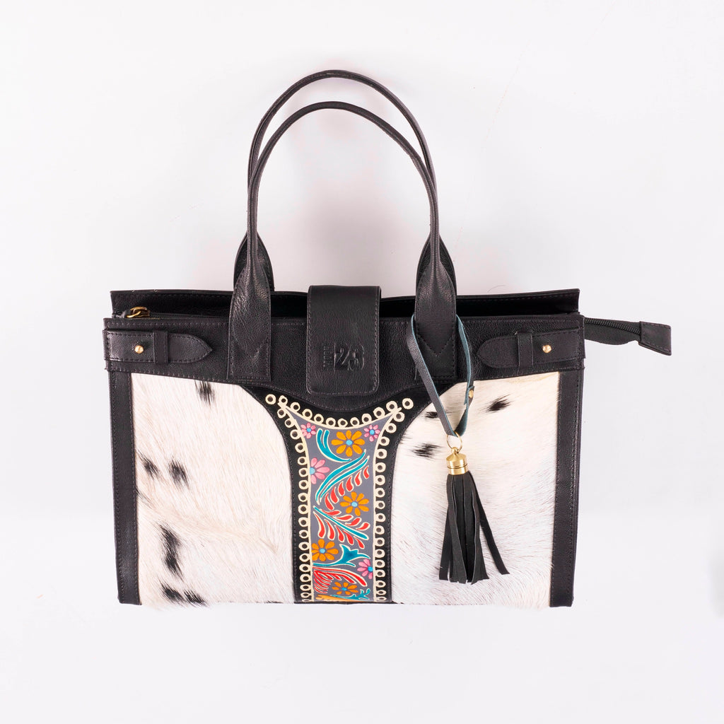 Structured leather tote bag front view showing cowhide panels, hand-painted floral embroidery, stud detailing and black leather tassel